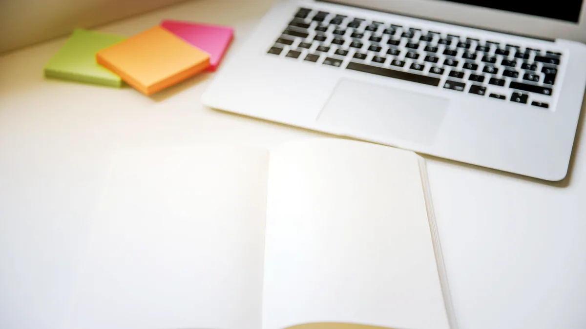 An open technical book beside a laptop with handwritten notes on the desk.